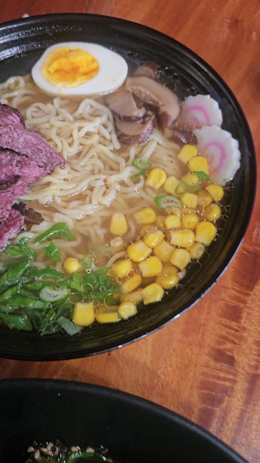 검은색 그릇에 담긴 라멘. 옥수수, 계란, 고기, 해초 등 다양한 재료가 보인다.