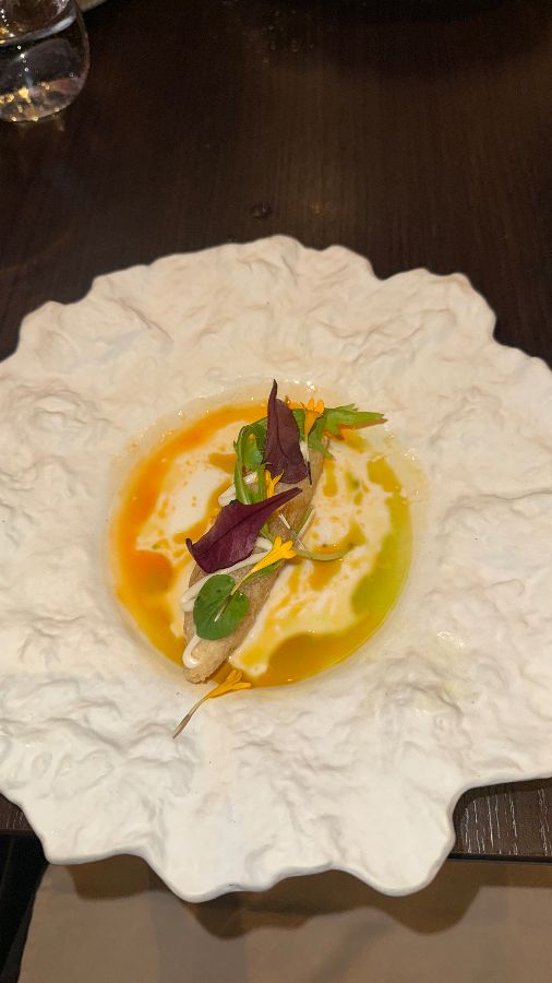 오렌지색과 녹색 소스가 어우러진 요리, 흰색 꽃잎 모양의 접시에 담겨 있다.