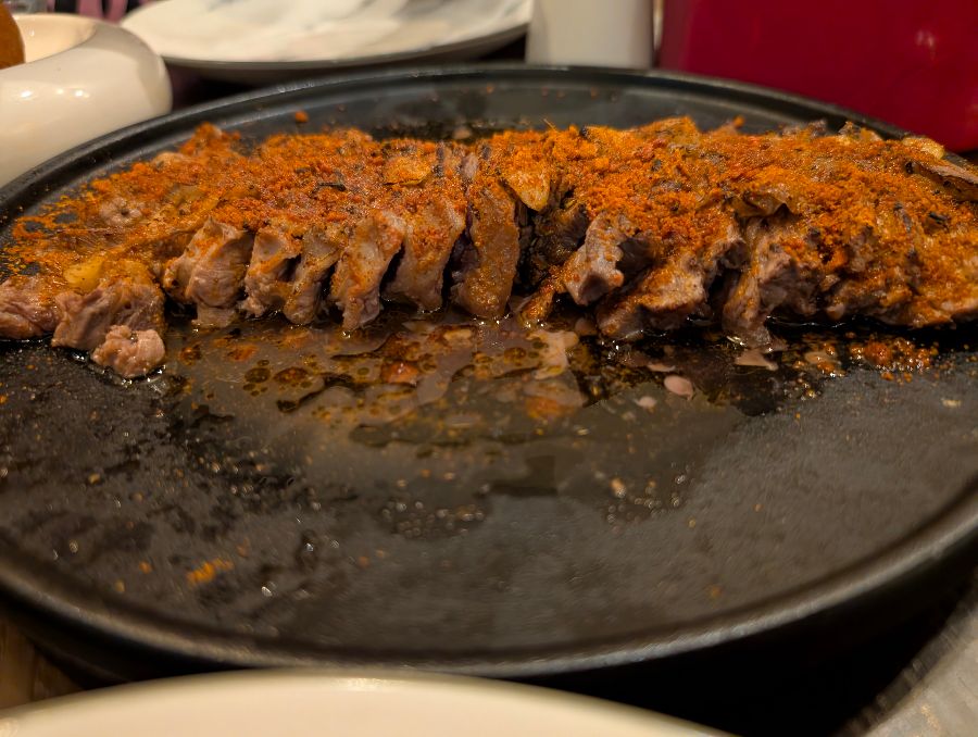 철판에 담긴 양념된 고기 요리, 붉은색 양념이 고기 위에 고르게 뿌려져 있다.