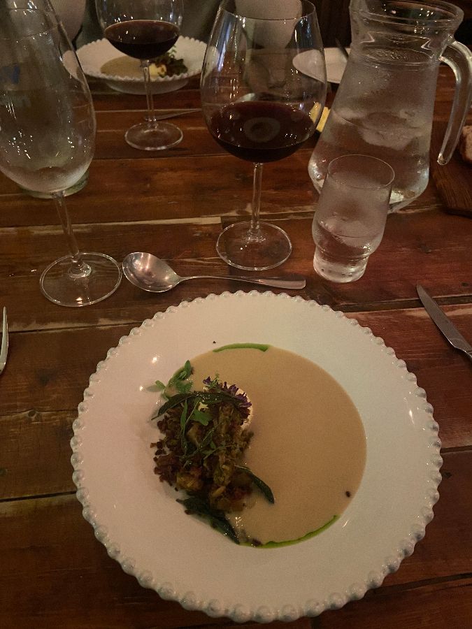 테이블 위에 놓인 음식 사진. 접시 위에 크림색 수프와 채소가 올려져 있다.