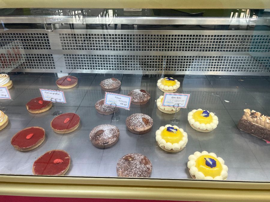 다양한 종류의 페이스트리들이 진열되어 있는 쇼케이스 내부의 모습. 빨간색 딸기 타르트, 노란색 레몬 타르트, 초콜릿 무스 케이크 등 다채로운 색상과 모양의 디저트들이 가지런히 놓여 있어 시각적인 즐거움을 선사합니다.