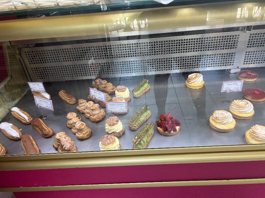 쇼케이스에 진열된 다양한 페이스트리들. 에클레어, 타르트, 그리고 슈가파우더가 뿌려진 페이스트리 등 여러 종류의 달콤한 디저트가 유리 너머로 시선을 사로잡습니다.