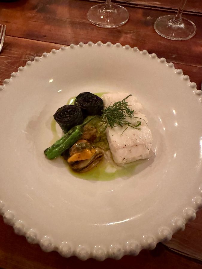 테이블 위에 놓인 음식 사진. 흰색 접시에 생선 요리와 채소가 올려져 있다.