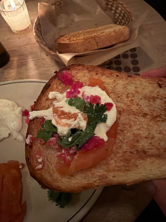 빵 위에 연어, 케이퍼, 채소, 크림치즈를 올려 먹는 모습