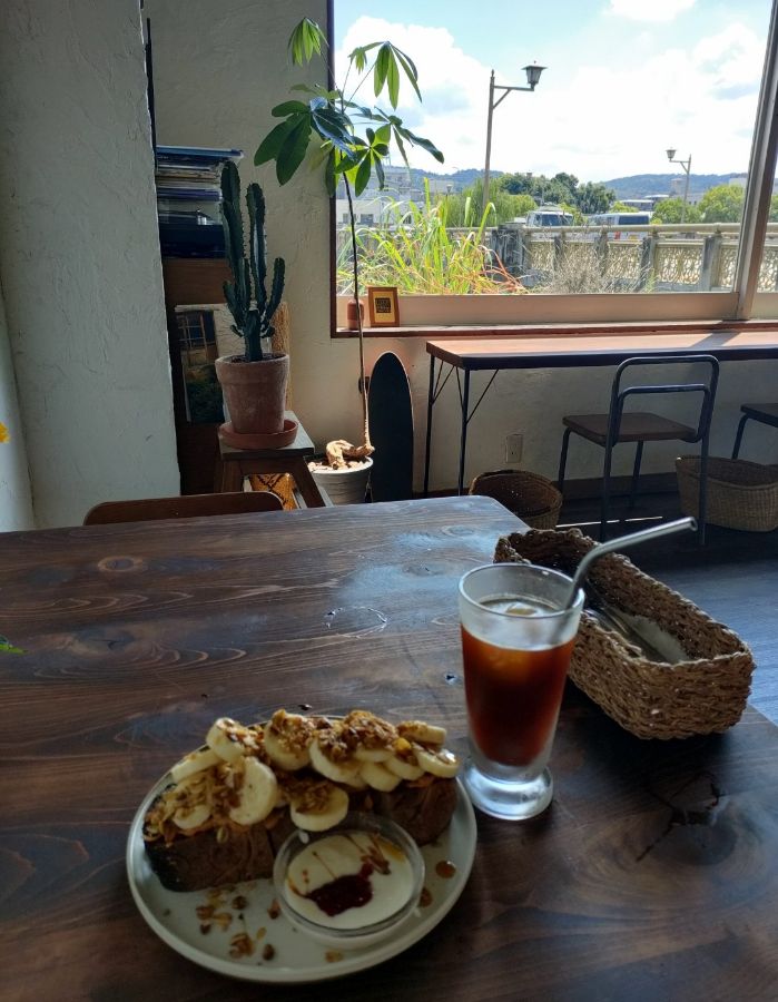 창밖 풍경이 보이는 테이블 위에 놓인 피넛버터 바나나 오픈 샌드위치와 아이스 커피